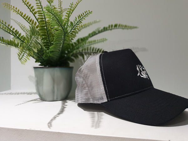 Side ways photograph of snapback trucker's cap in black and grey with The Cally Collection logo in white.