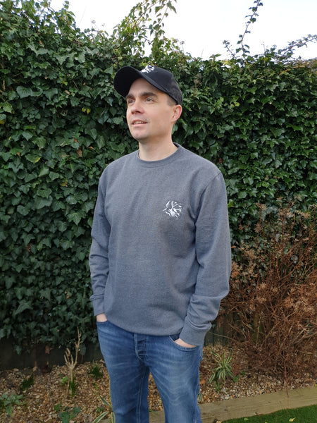 Photo of man wearing a dark grey sweatshirt with The Cally Collection logo in white in the top left corner.  The man is also wearing a black trucker's cap with The Cally Collection logo in white on the front panel.