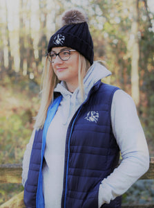 Photo of lady wearing a light grey hoody from The Cally Collection, with a navy gilet with navy trim and The Cally Collection logo in white in the top left corner.   The lady is also wearing a black chunky beanie with a pom pom on the top, and The Cally Collection logo in white at the front.