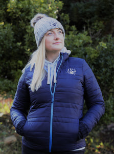 Photo of lady wearing a light grey hoody from The Cally Collection, with a navy lightweight jacket with navy trim and The Cally Collection logo in white in the top left corner.   The lady is also wearing a light grey chunky beanie with a pom pom on the top and The Cally Collection logo in black at the front.