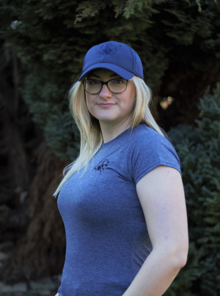 Photo of lady wearing dary grey t-shirt with The Cally Collection logo in black in the top left corner.   The lady is also wearing a navy air mesh cap with The Cally Collection logo in navy on the front panel.