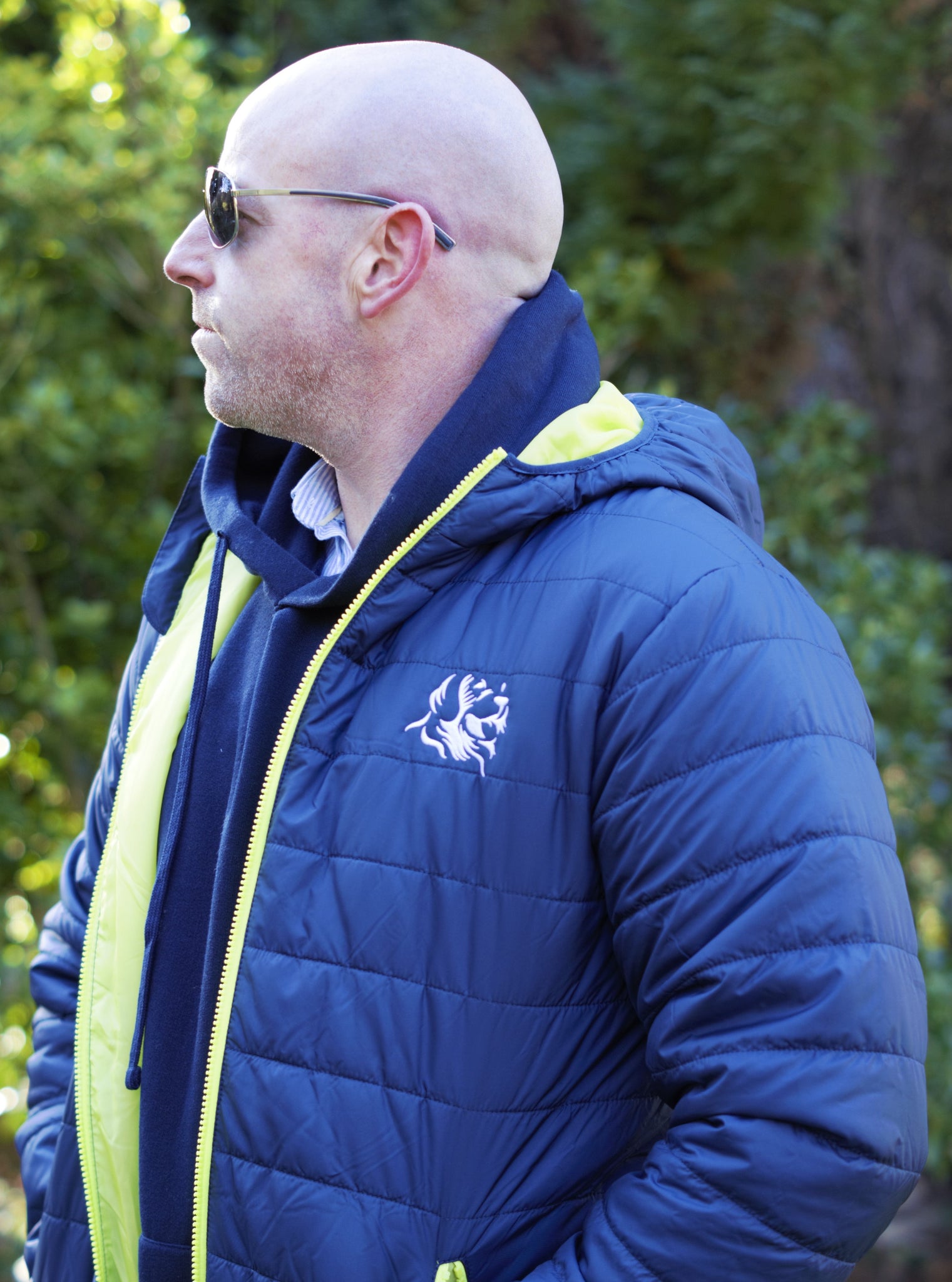 Photo of man wearing a navy hoody from The Cally Collection, with a navy lightweight jacket with lime trim and The Cally Collection logo in white in the top left corner.