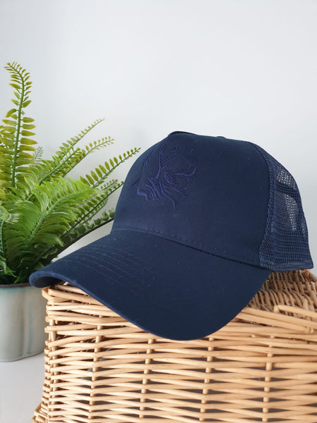 Photo of navy trucker's cap with The Cally Collection logo in navy on the front panel. 